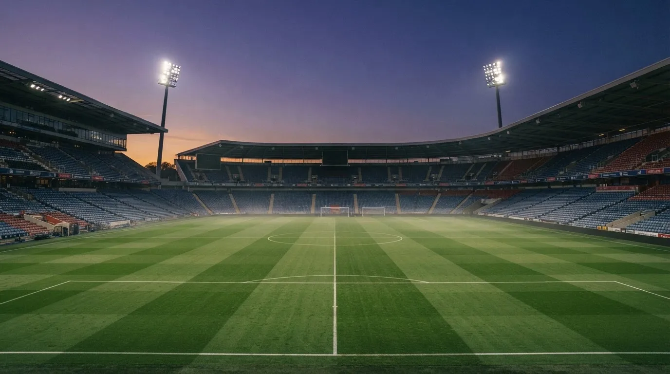 An empty football stadium with floodlight masts at dusk