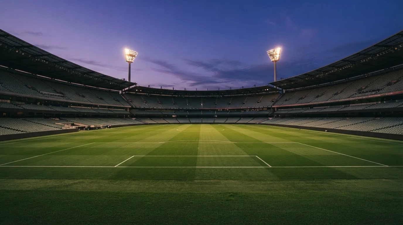 An empty football stadium with floodlight masts at dusk
