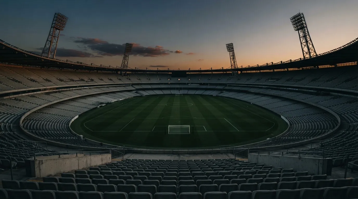 An empty football stadium with floodlight masts at dusk
